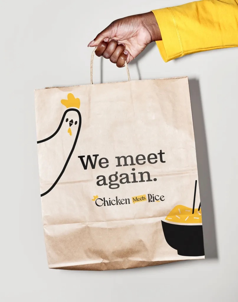 Person holding Chicken Meets Rice bag, showing off the branding.