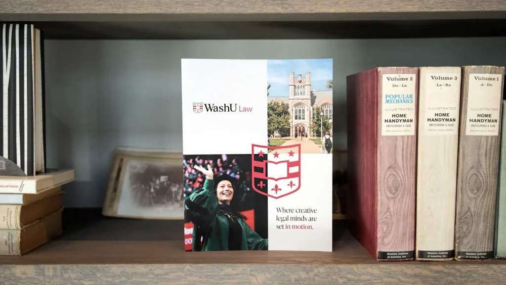 WashU Law admissions brochure displayed on bookshelf featuring campus imagery and branded shield design by Atomicdust.